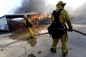 Firefighters try to protect surrounding homes earlier this month as they battle the Sandalwood Fire in the Villa Calimesa Mobile Home Park in Calimesa, Calif. A deadly blaze that tore through the Southern California mobile home community this month started when a trash truck caught fire and the driver dumped the burning garbage on the side the road. Now, the waste industry is reviewing longstanding guidance to drivers to dump burning trash to ensure their safety, limit truck damage and prevent explosions. Photo by Jennifer Cappuccio Maher of The Orange County Register/SCNG via AP